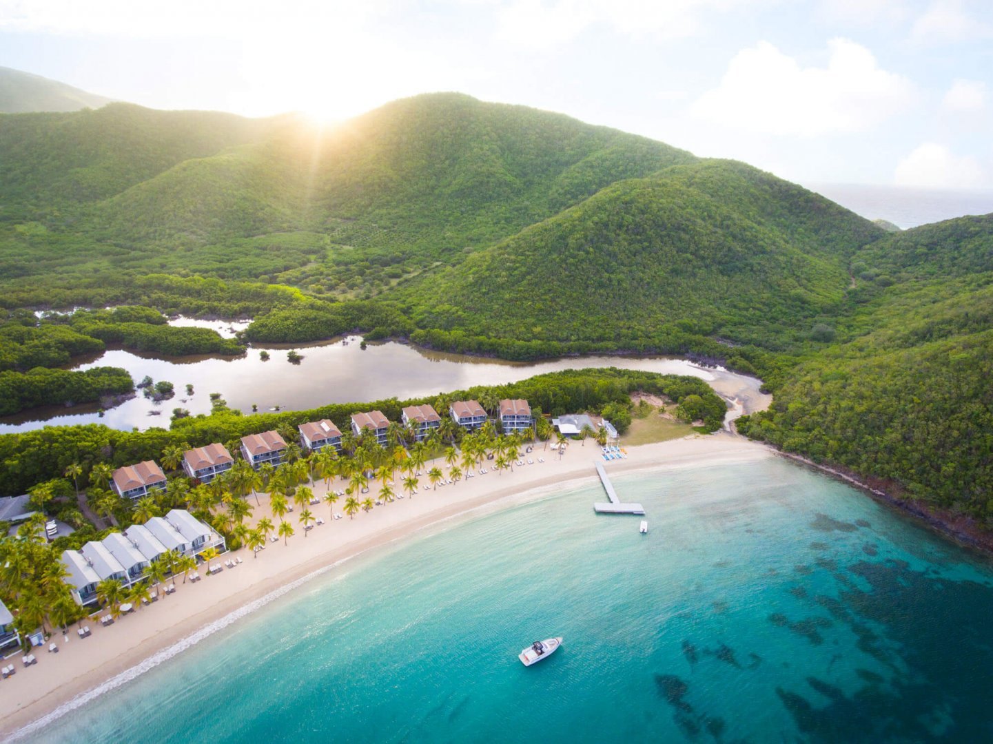 Aerial view of a row of beach cottages between a mangrove lagoon and a clear turquoise bay