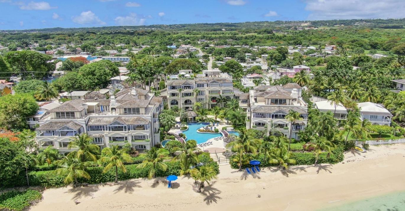 Aerial view of beachfront condominium buildings with a pool garden and sandy shoreline