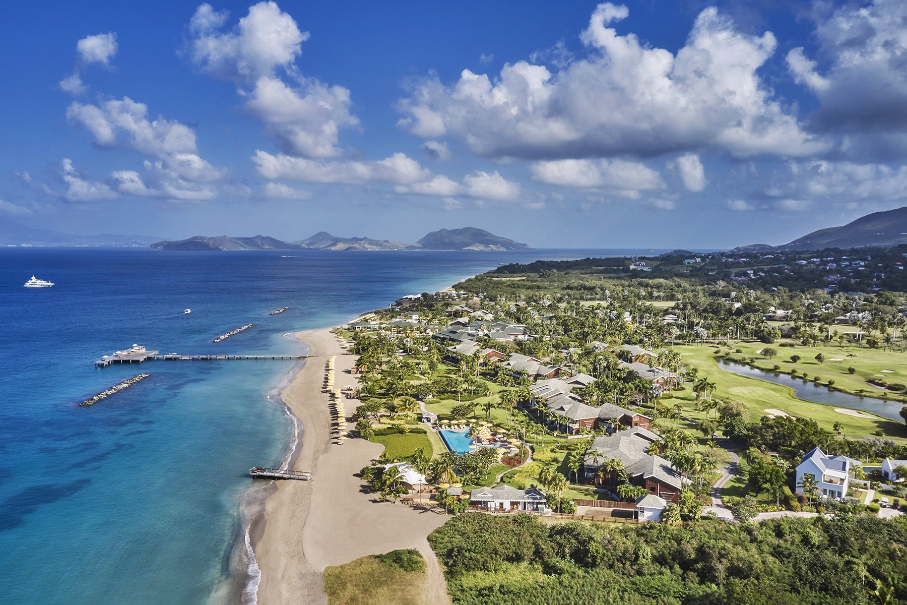 Aerial view of the Four Seasons Resort Nevis villas, golf course and pier along Pinney's Beach, with St Kitts across The Narrows