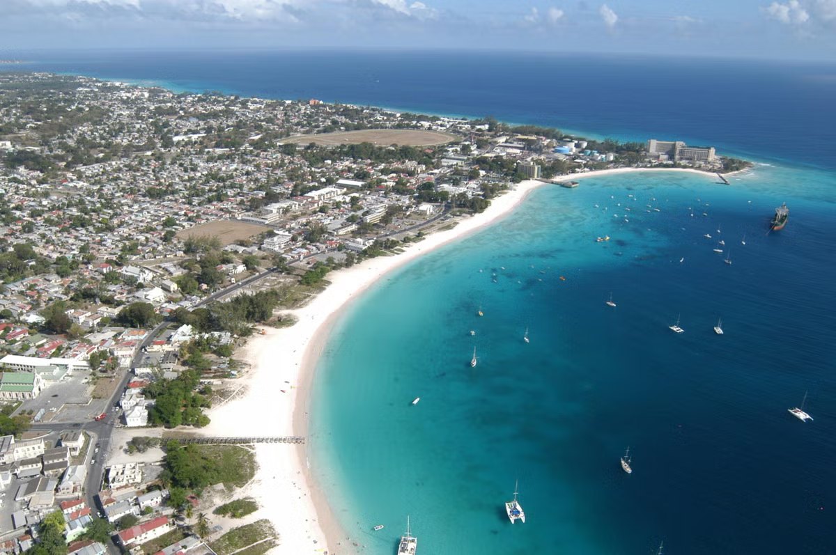Aerial view of a wide sandy bay full of moored yachts beside a dense coastal town
