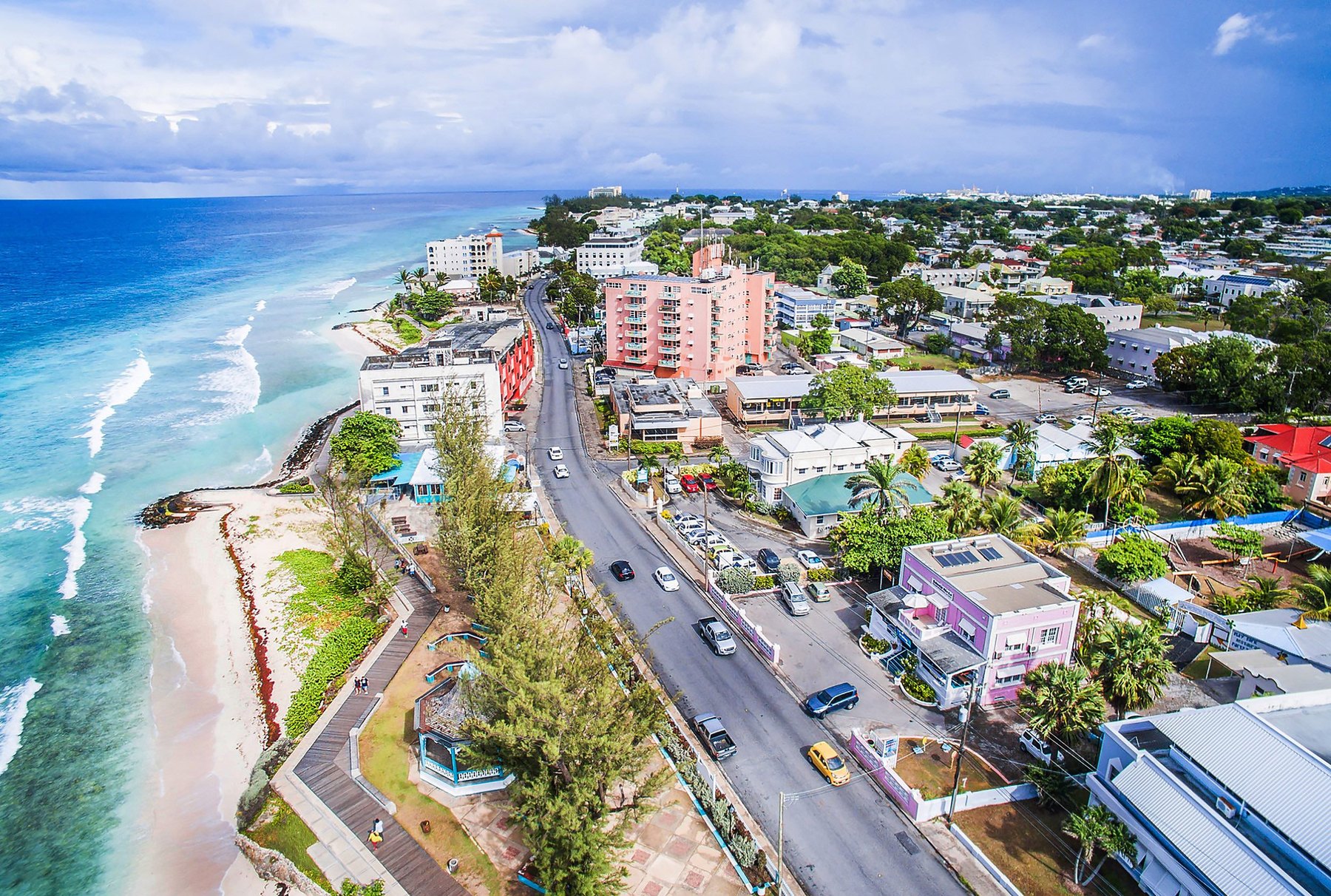 Aerial view of a coastal road, low-rise buildings and a surf-fringed town beach