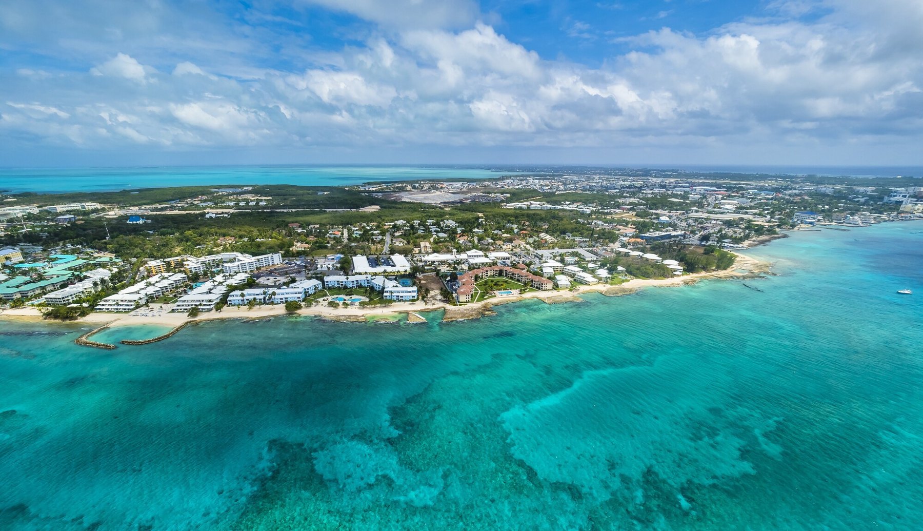 Aerial view of turquoise reef water beside a low-rise beachfront resort strip