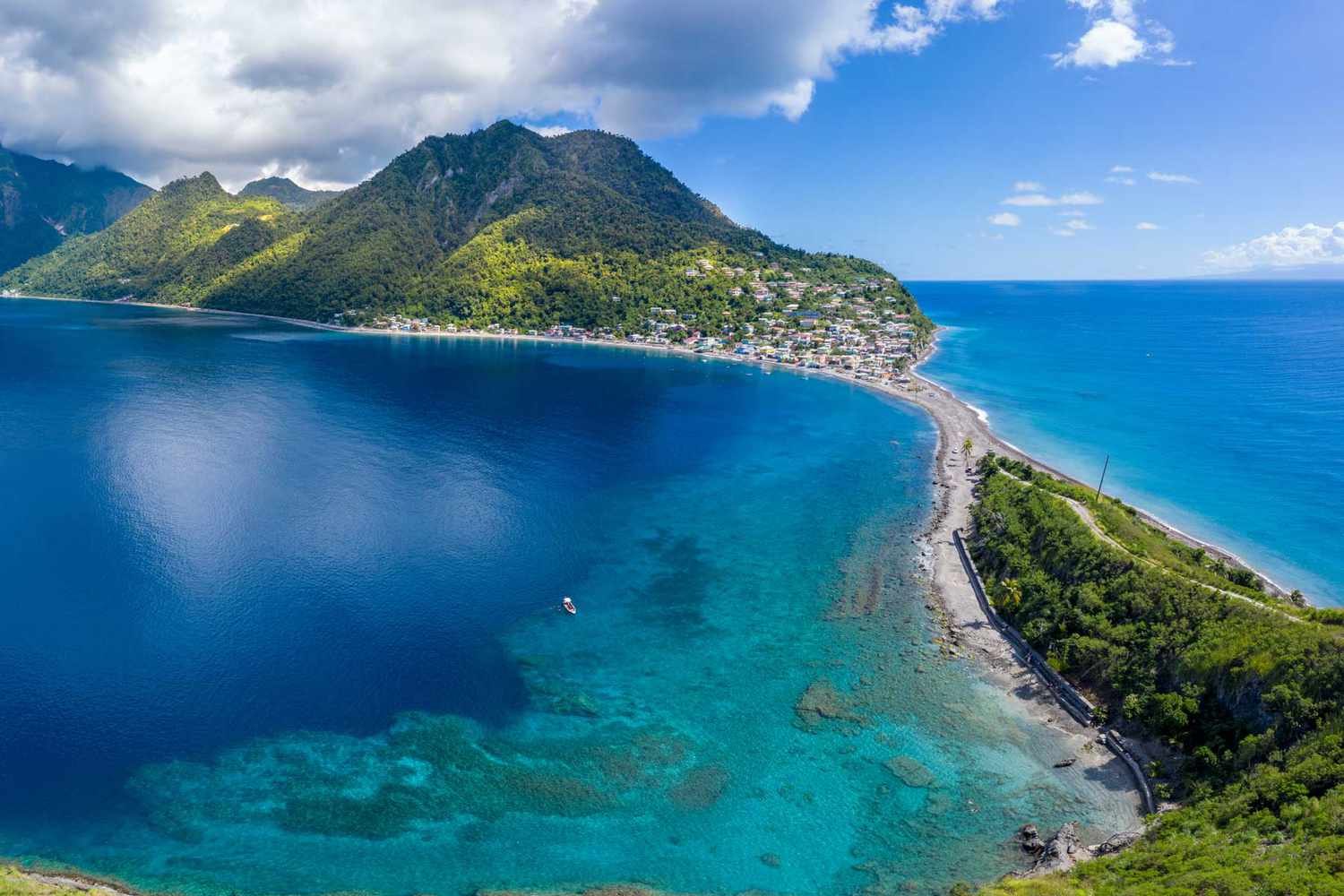 Green mountain village on a curving shoreline between deep blue and turquoise water.