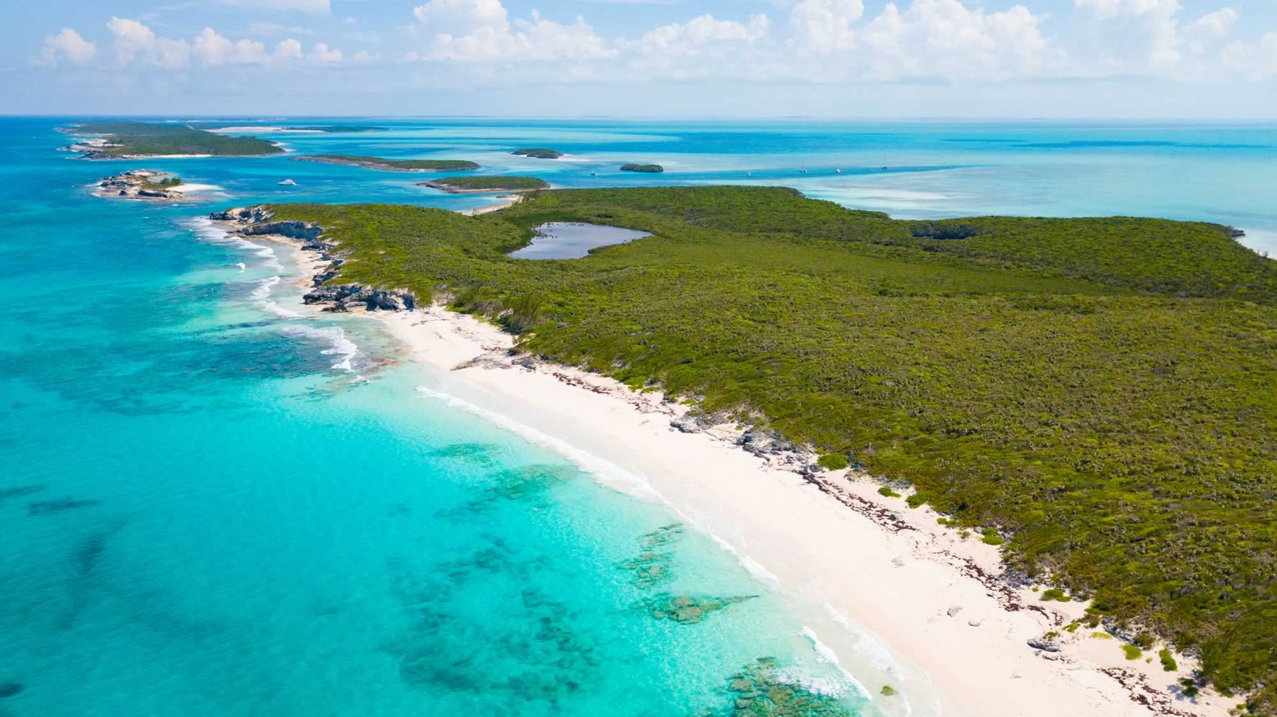 Aerial view of an empty curving beach along a scrub-covered cay with turquoise shallows