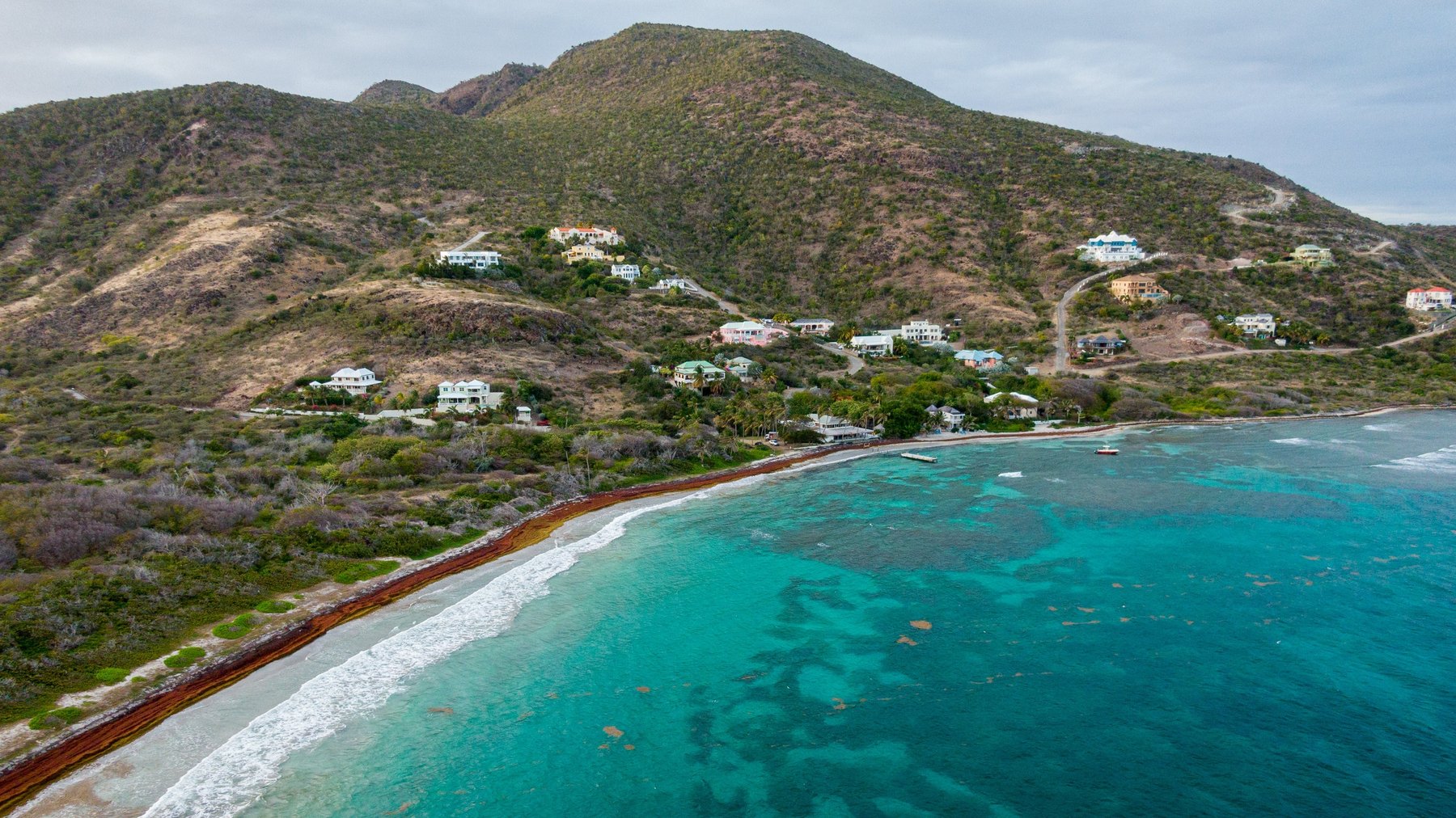 Aerial view of scattered hillside homes on a dry ridge above a shallow turquoise reef