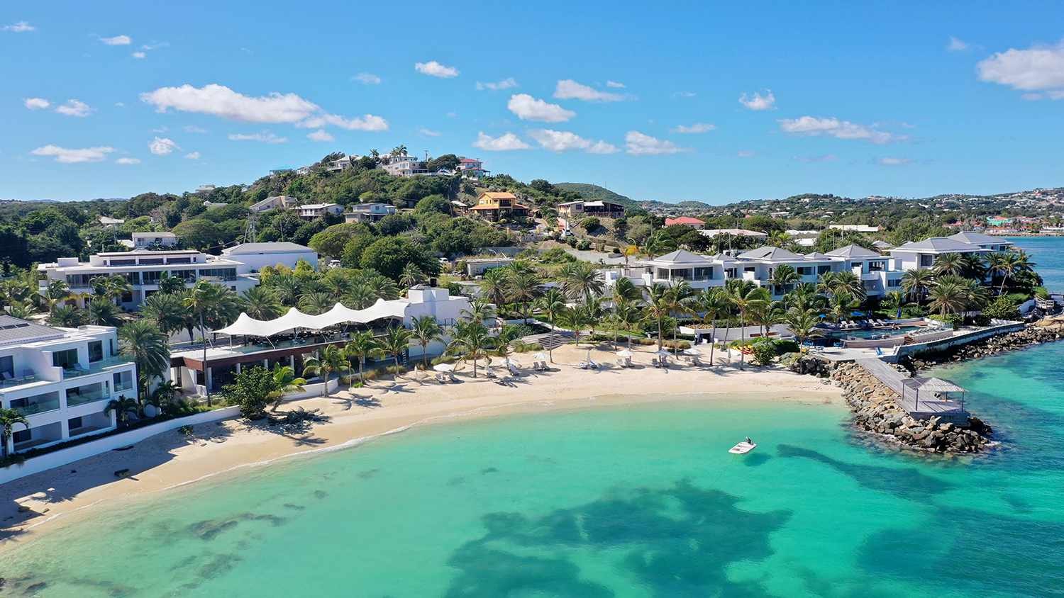 Aerial view of contemporary white villas around a small sand cove with clear turquoise water