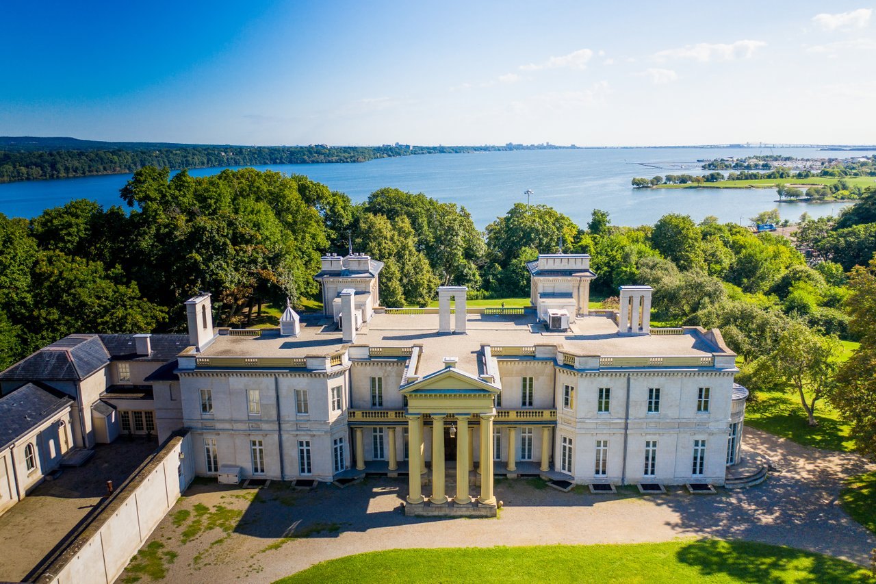Aerial view of a grand neoclassical stone estate overlooking a wide bay