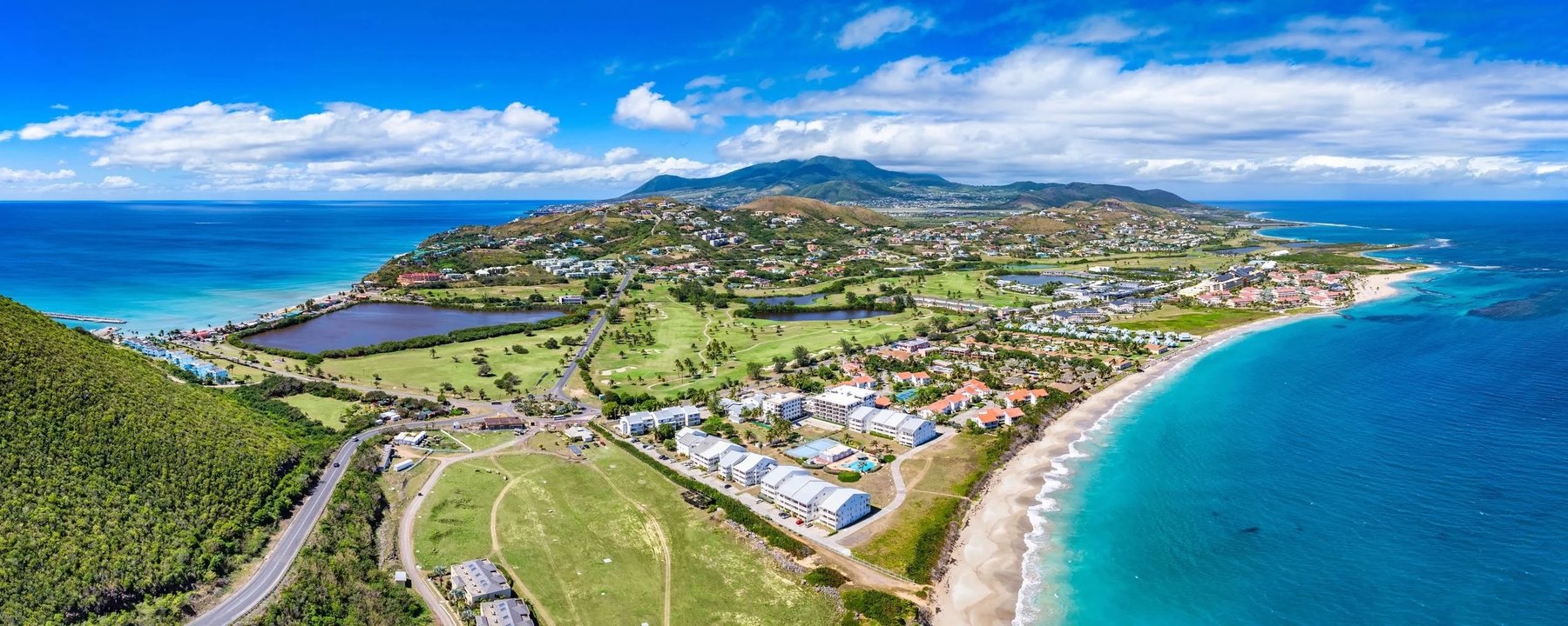 Wide aerial panorama of a coastal peninsula with golf fairways, resorts and a curving sand beach