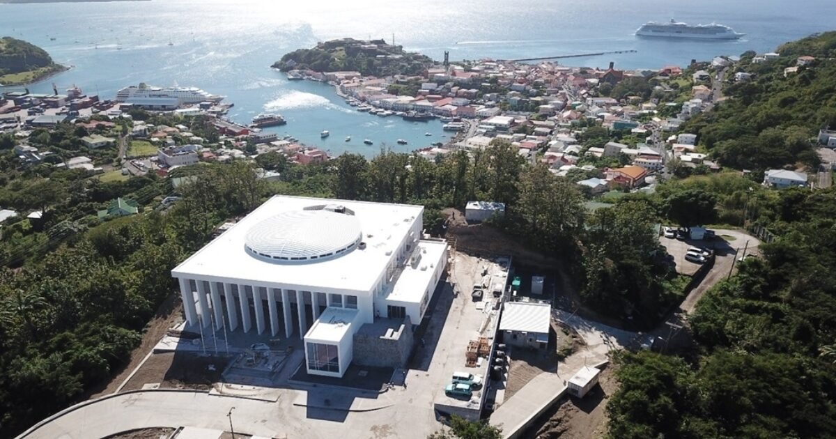 Drone view of a white colonnaded public building on a ridge above a cruise harbour