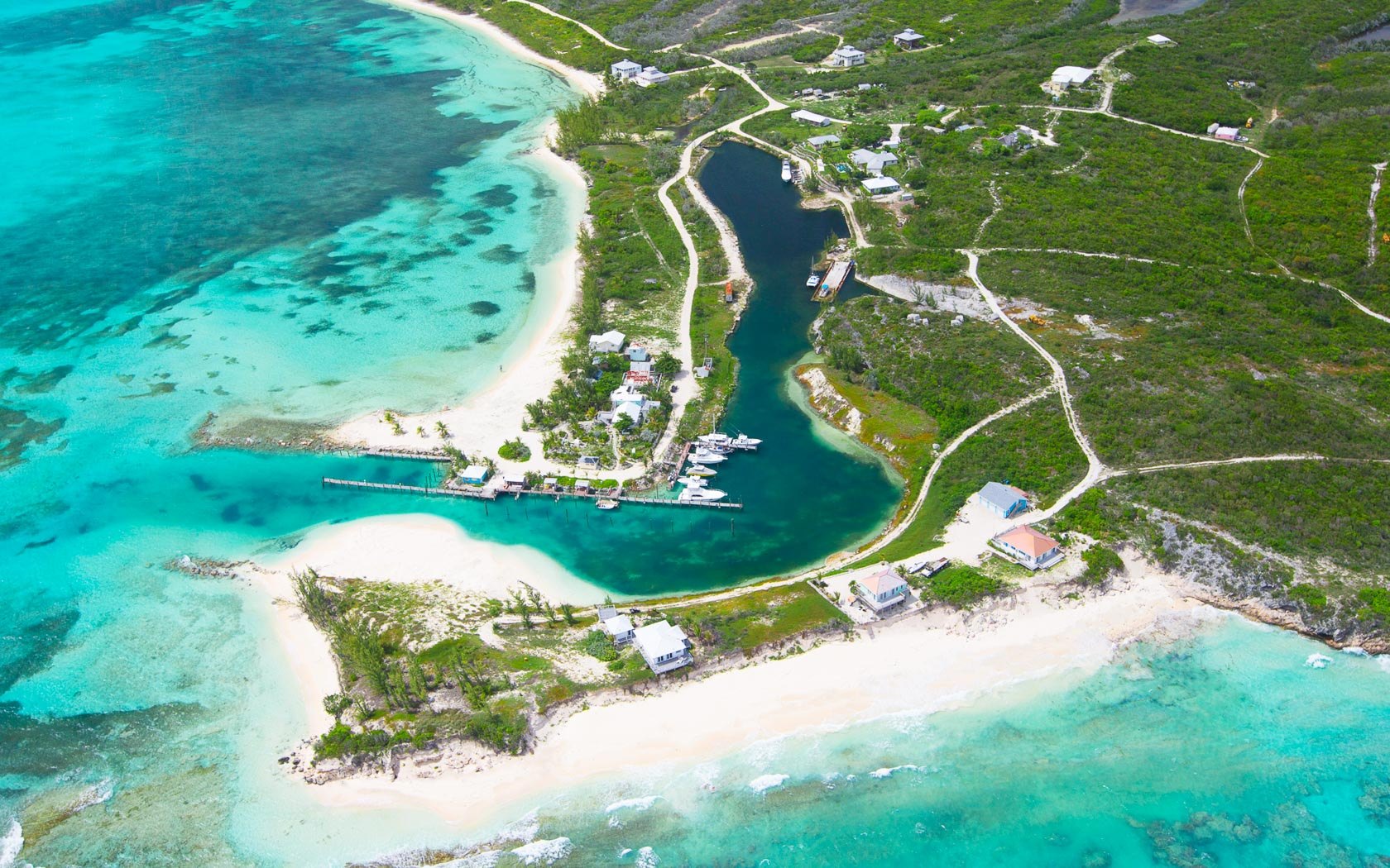 Aerial view of a sheltered inland marina and boats between two curving white beaches