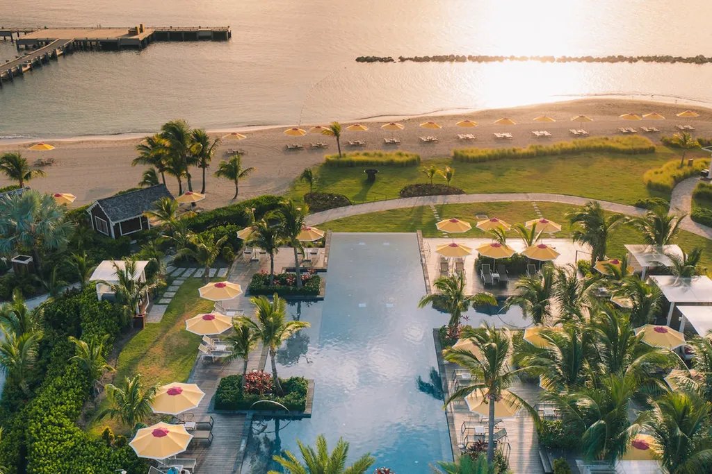 Aerial view of a resort pool, palms and an umbrella-lined beach at sunset