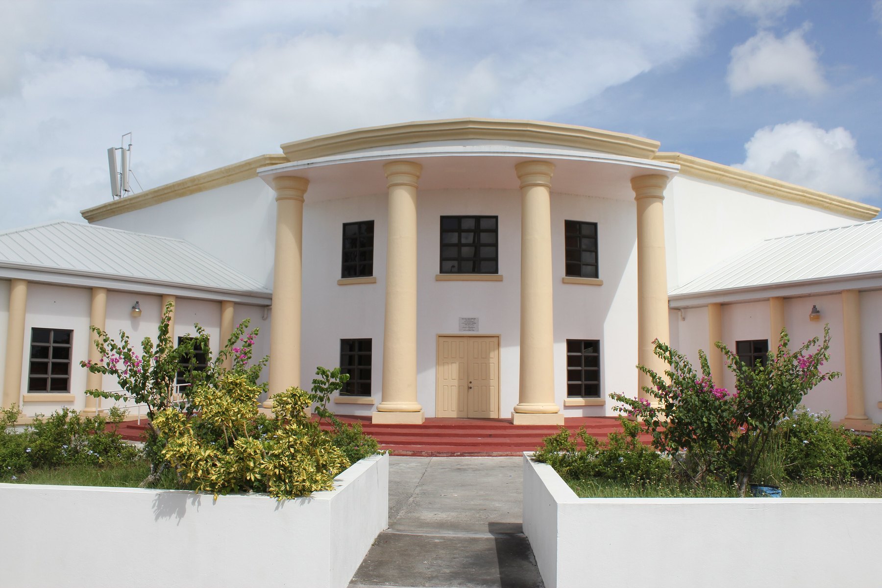 Pink and cream parliament building with columned portico, red steps and flowering shrubs