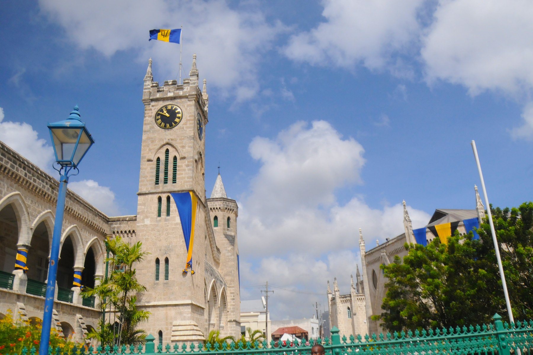 Gothic stone clock tower flying the Barbados flag above blue and gold bunting