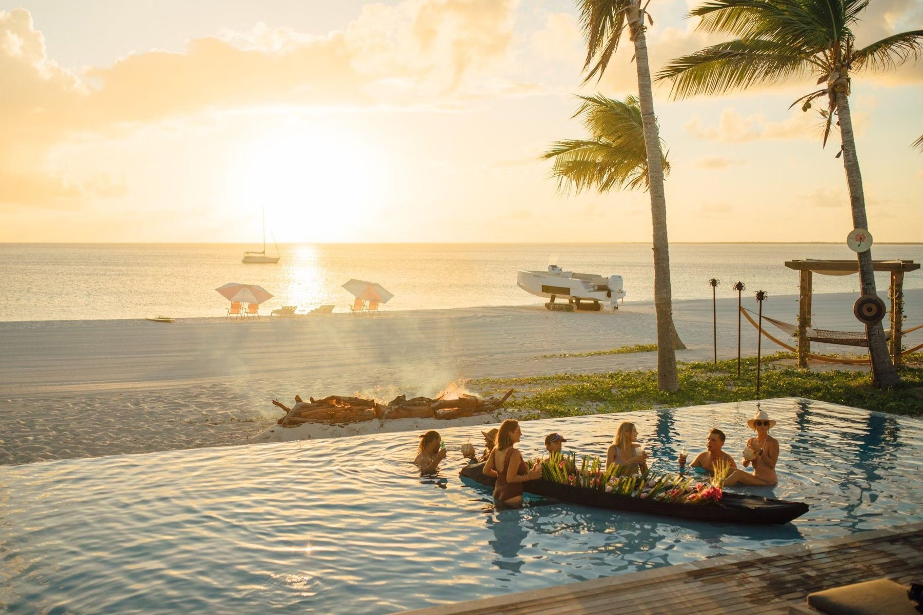 Guests at Barbuda Ocean Club's beach club pool with floating canoe bar at sunset