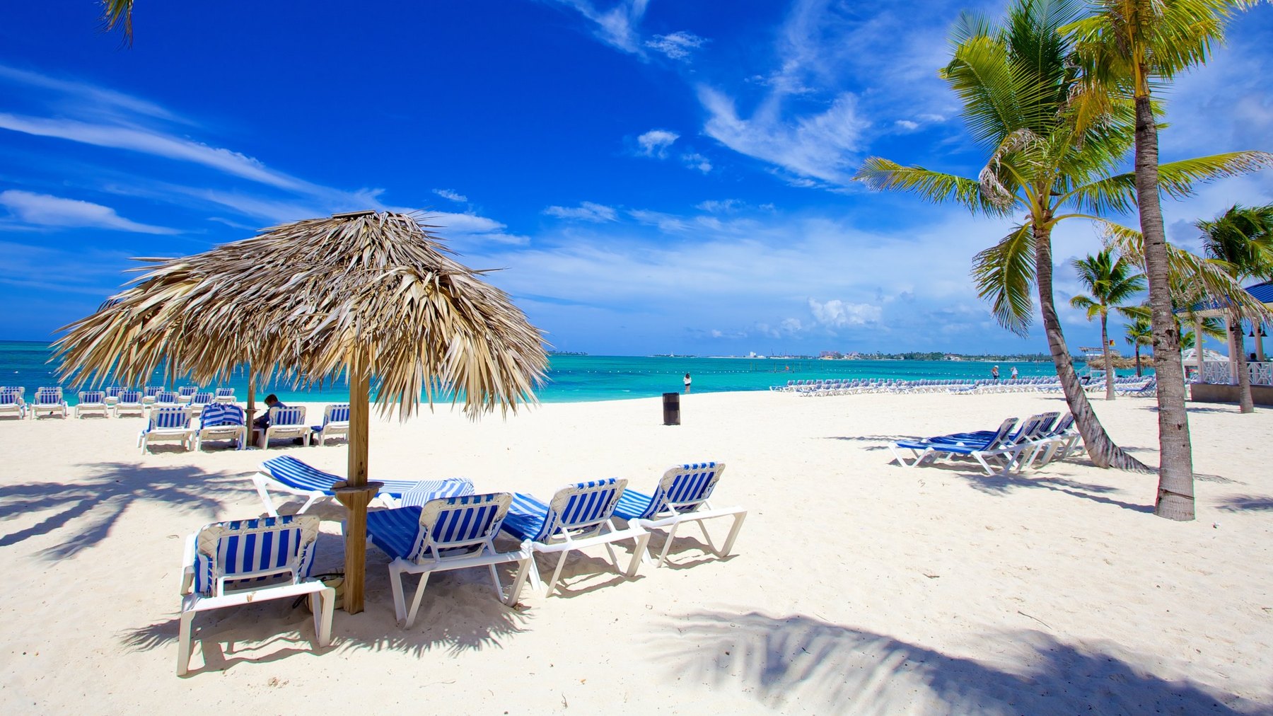 Blue striped loungers under a thatched umbrella on white sand beside calm turquoise sea