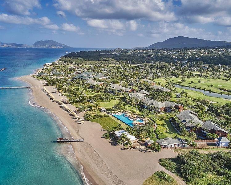 Aerial view of low-rise beachfront buildings, palms and a golf course beside the sea