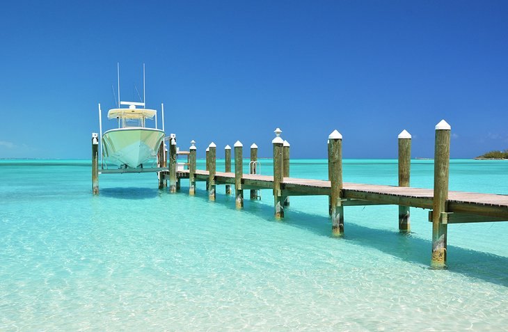 A centre-console boat raised on a lift beside a wooden pier in clear shallow water