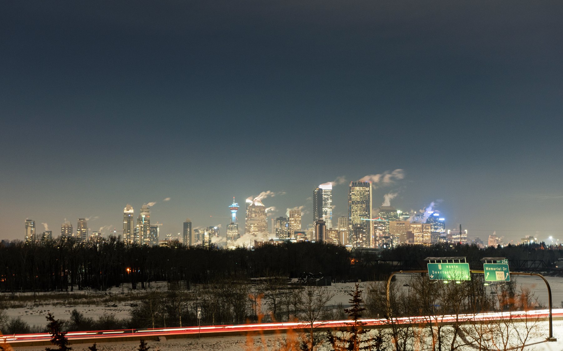 Calgary skyline glowing on a cold winter night above a snow-lined highway