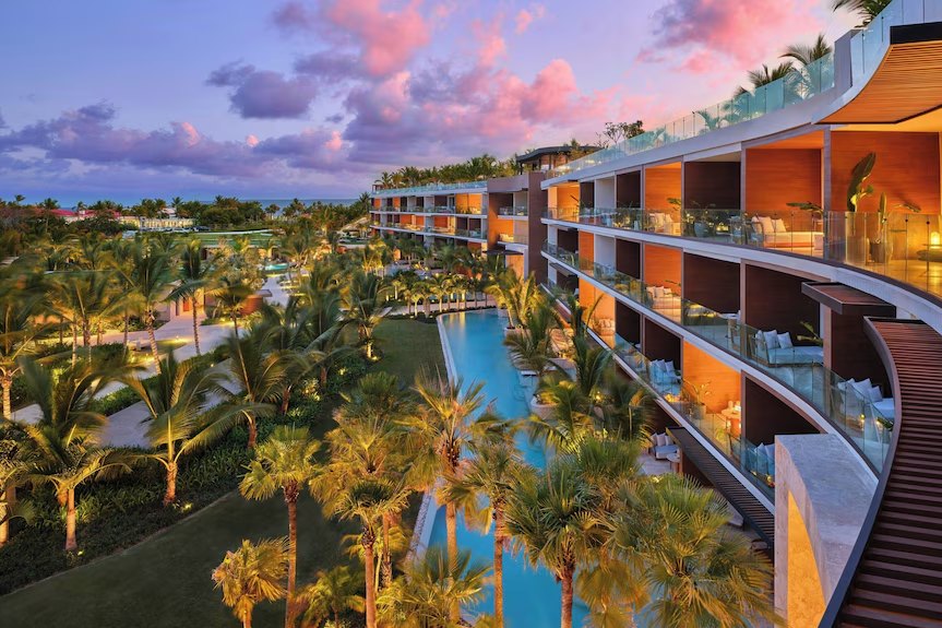 Curved oceanfront residence building and palm-lined pool at sunset, St Regis Cap Cana
