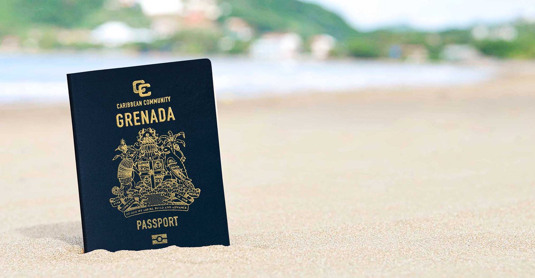 A Grenadian passport standing upright in the sand on a Grenada beach