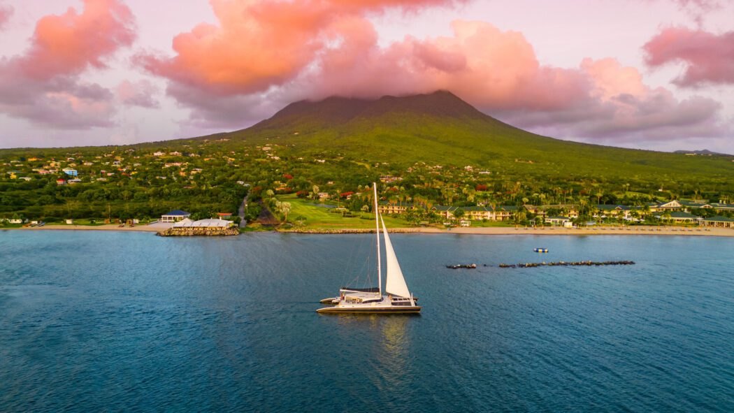 Catamaran anchored off the west coast of Nevis, the whole low-rise shoreline sitting beneath the single cloud-capped cone of Nevis Peak