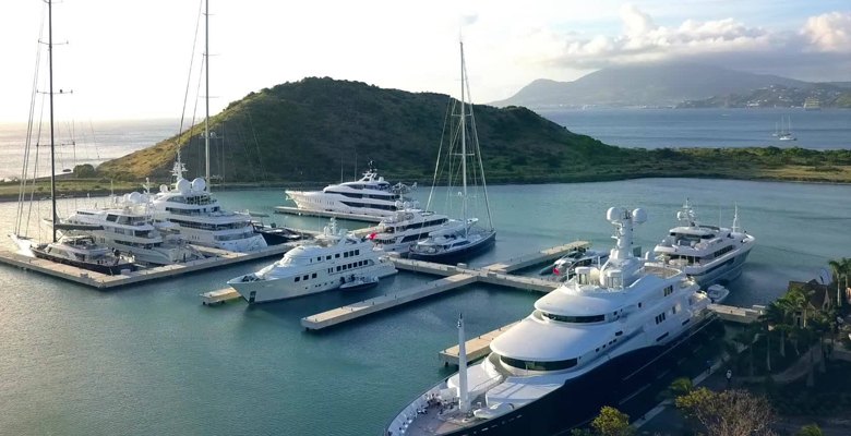 Row of superyachts along Christophe Harbour's marina docks, St Kitts, headland and open sea beyond