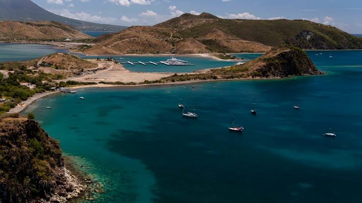 Sailboats anchored off the arid southeast peninsula of St Kitts, with the Christophe Harbour marina and the island's mountains beyond