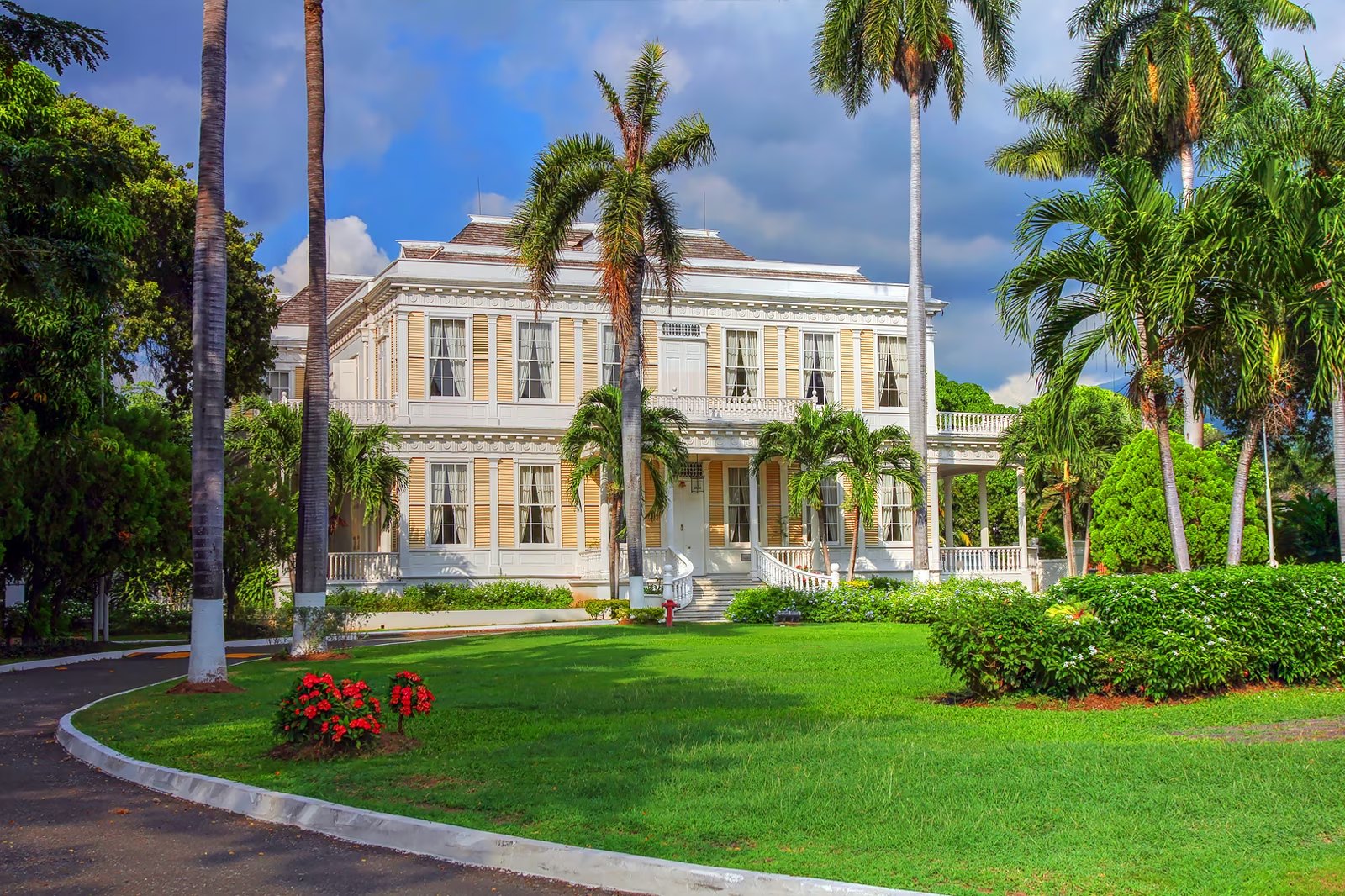 Two-storey colonial mansion with white balustrades framed by tall royal palms.