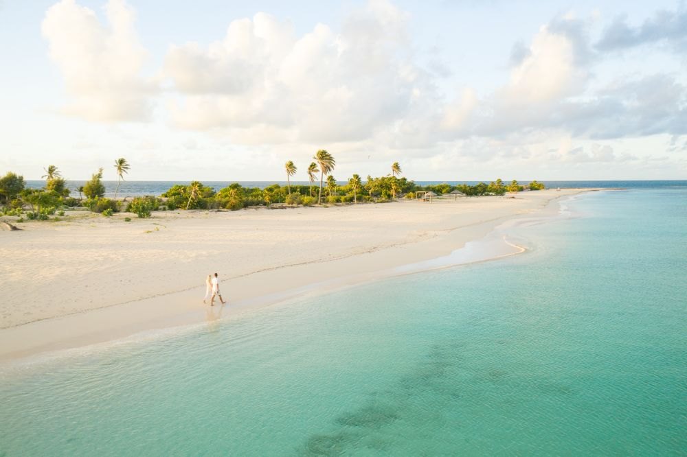 Couple walking a deserted sandbar in golden light beside pale green shallow water