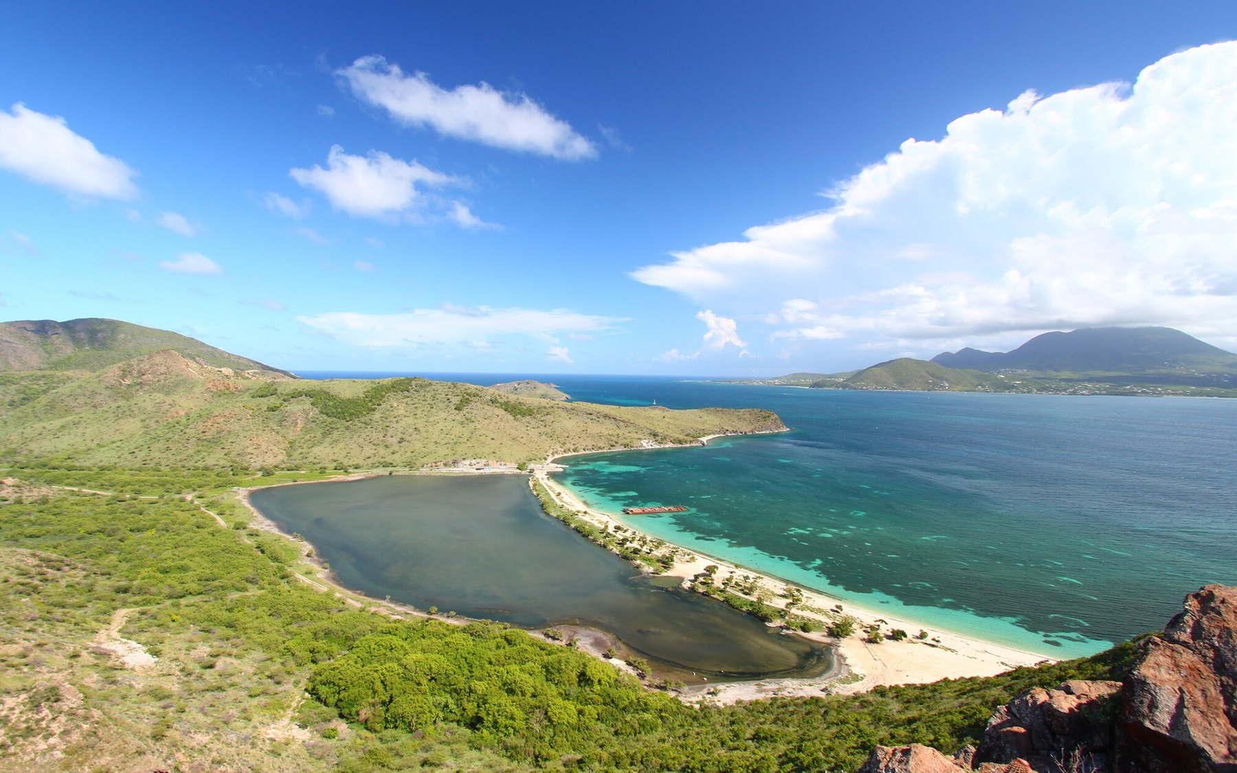 Elevated view of a curved sandy bay and green hills meeting clear turquoise sea
