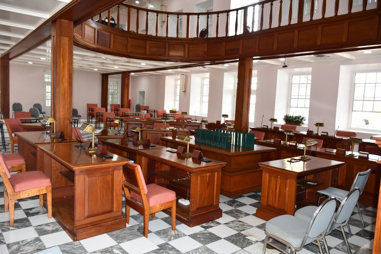Empty debating chamber with mahogany desks, brass lamps, pink chairs and a marble floor