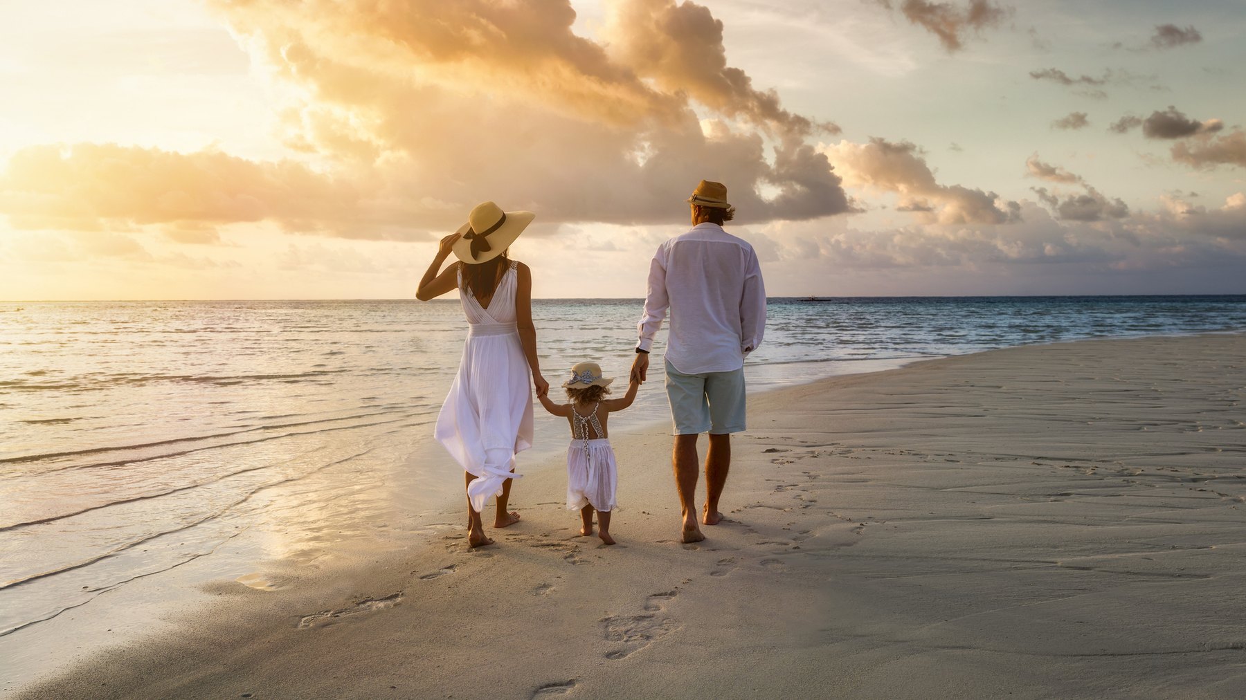 A couple and their young child walking a quiet beach at sunset