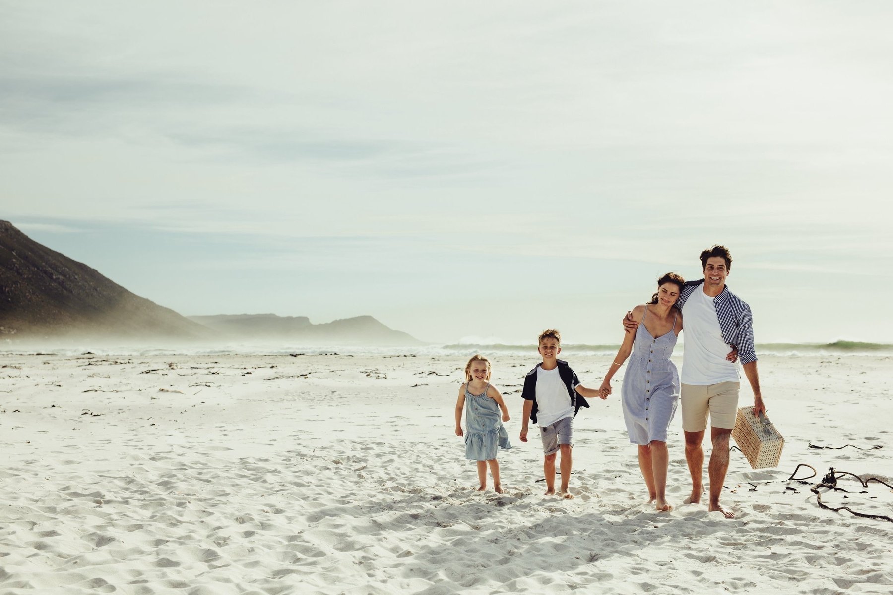 A family of four walking together along a wide, empty beach