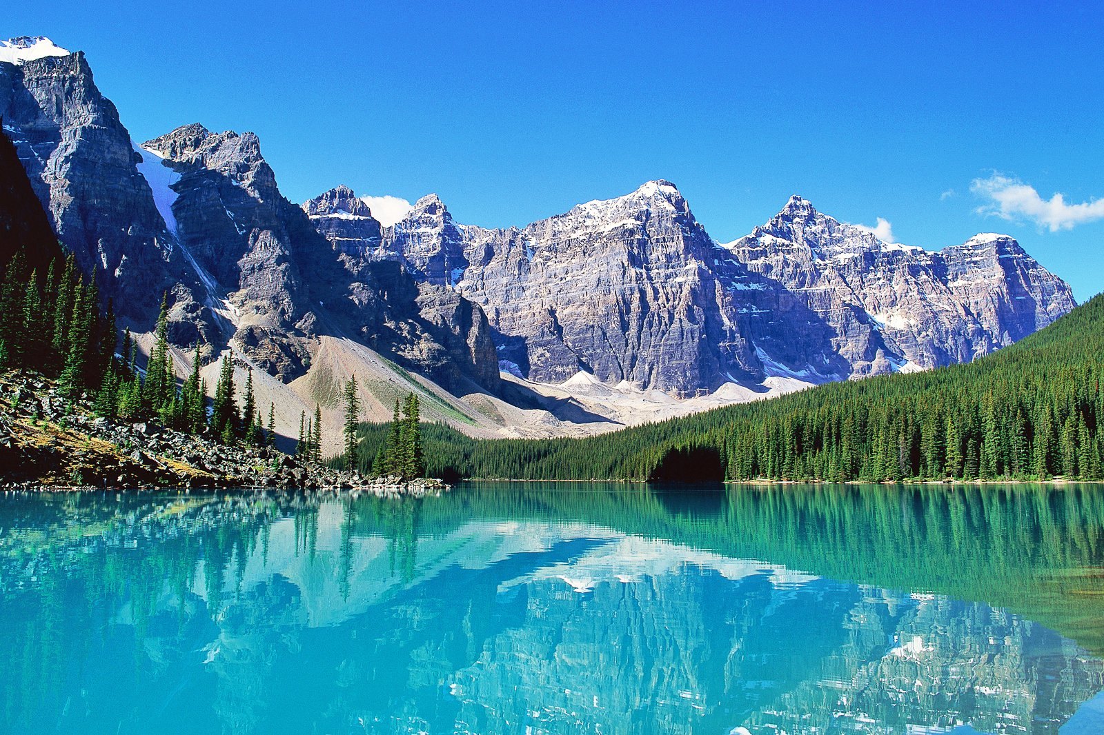 Turquoise glacial lake mirroring snow-dusted mountain peaks and dense evergreen forest