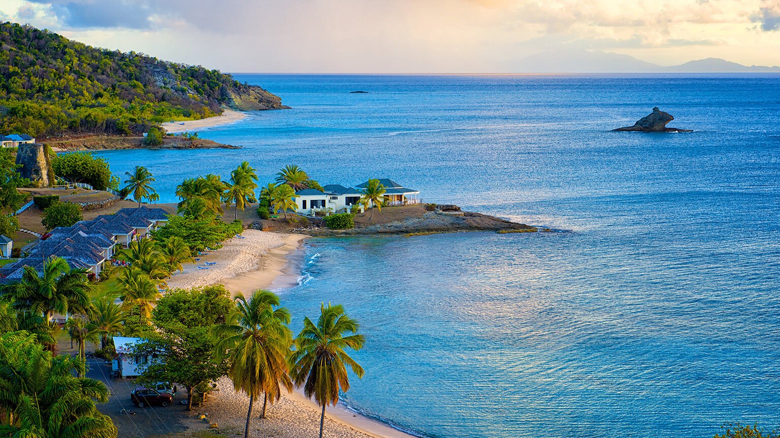 Warm evening light over a sheltered cove with palm-shaded villas and a rocky islet offshore
