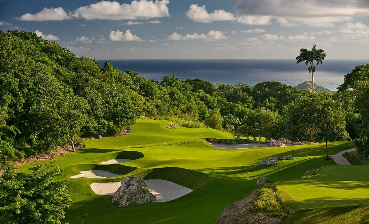 Manicured golf fairway and white bunkers framed by dense green hillside above the ocean