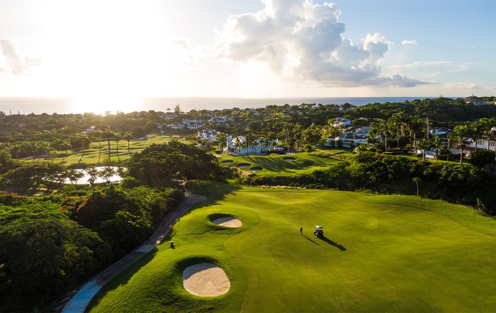 Aerial view of a manicured golf fairway and villas near the sea at sunset