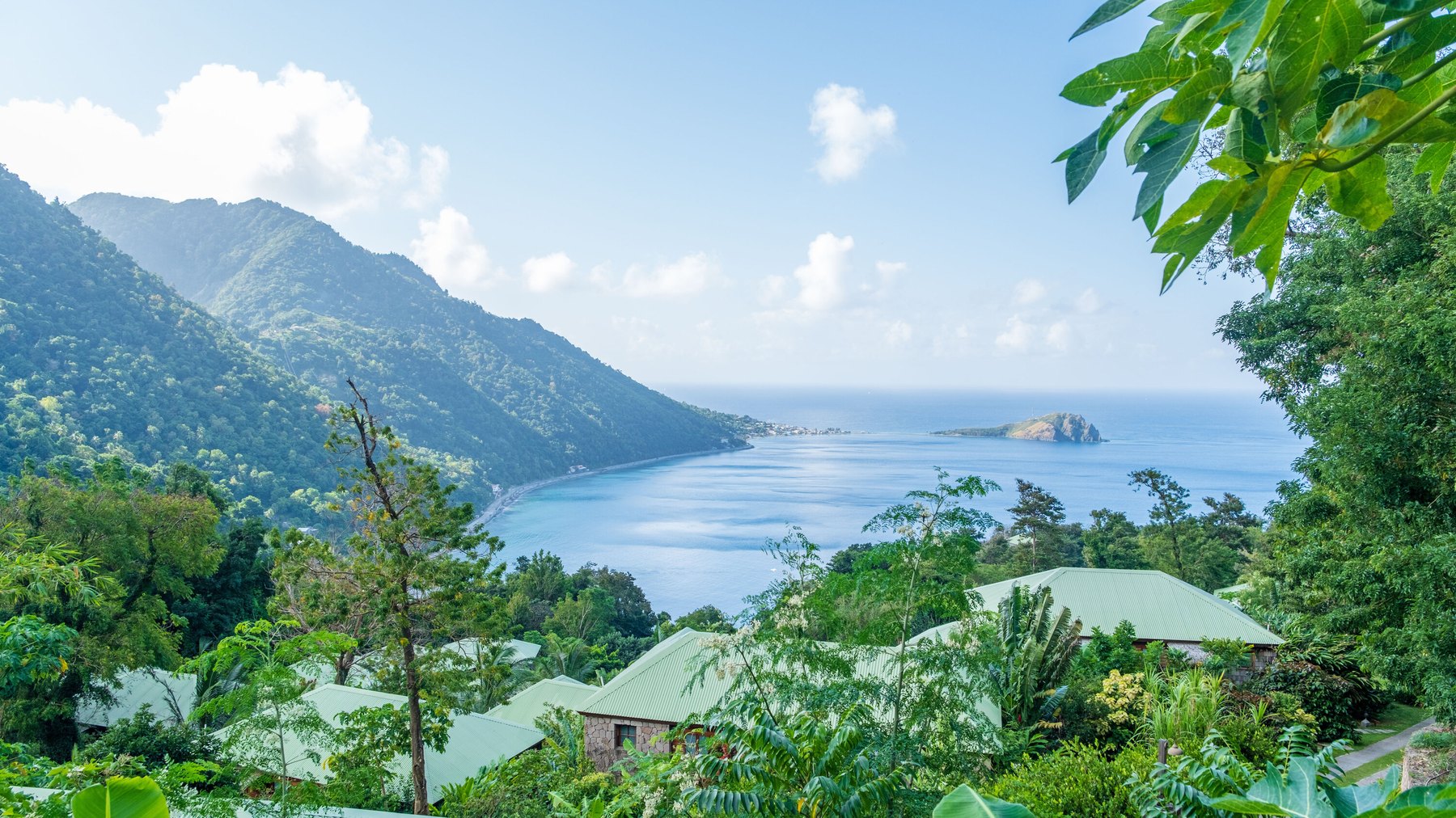 Green-roofed cottages built into forested hillside above a calm Caribbean bay