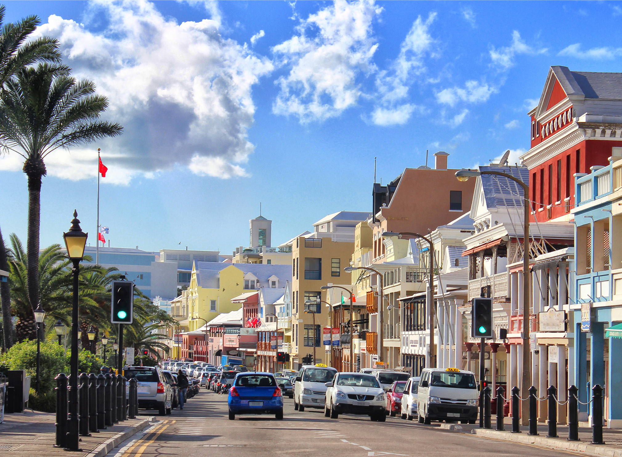 Front Street in Hamilton, Bermuda: a terrace of pastel colonial shopfronts under white stepped limestone roofs, with verandas, palms and taxis along the harbourfront.