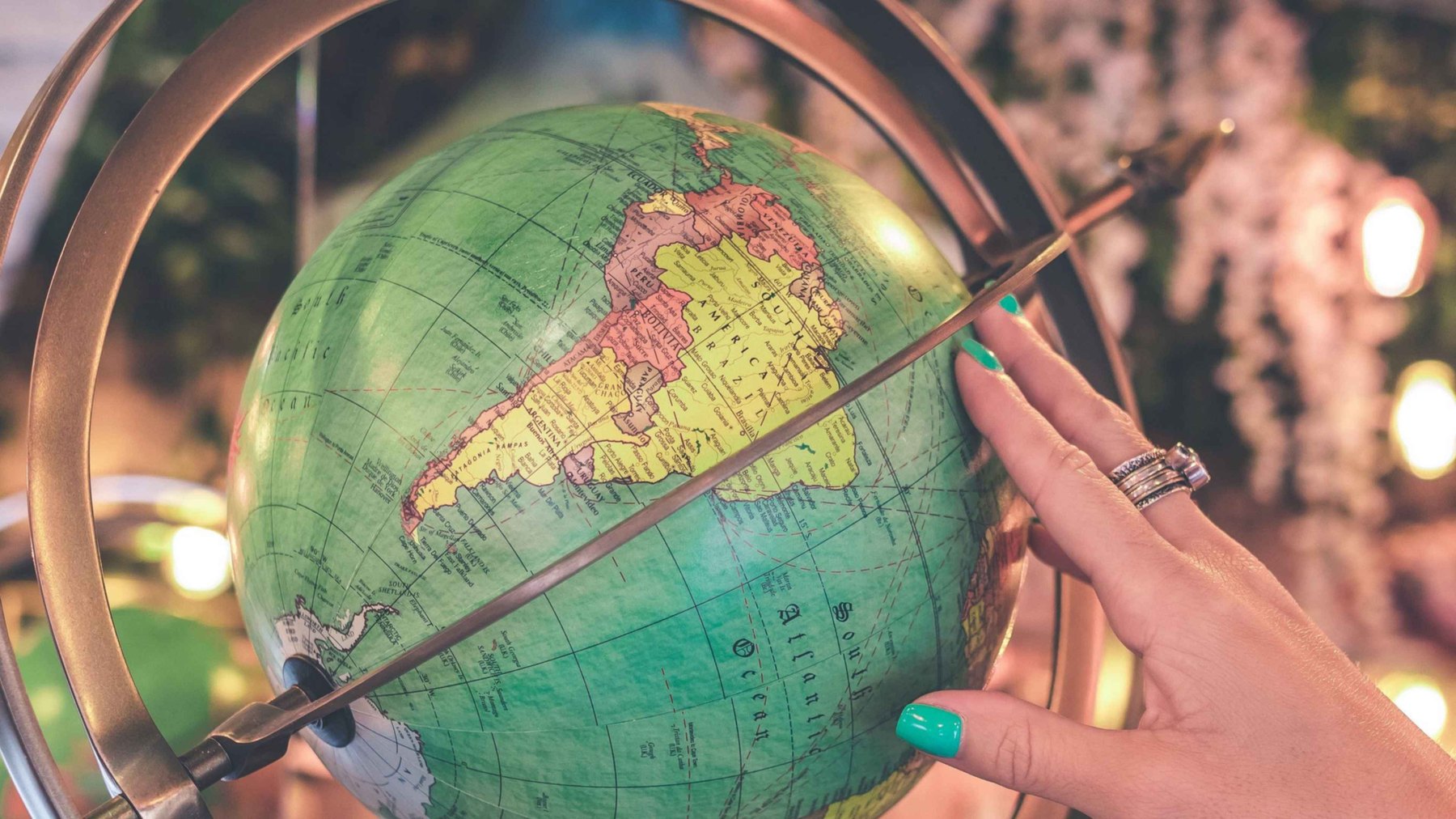 A hand with rings rests on a vintage desk globe amid warm bokeh lights