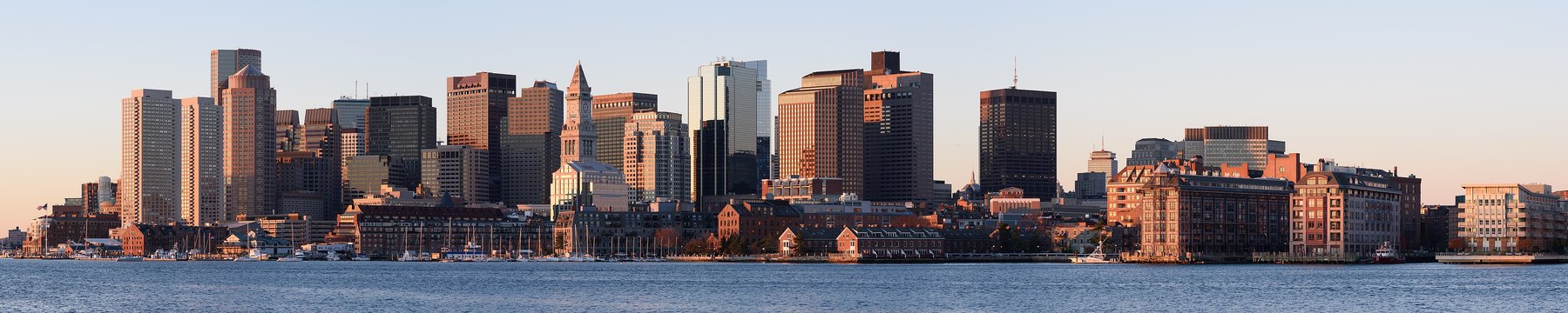 Wide harbour panorama of a downtown skyline lit by low golden sunrise light