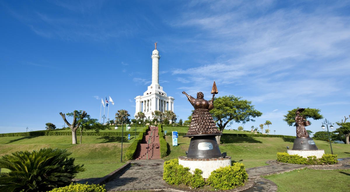 White stone monument on a grassy hill with bronze statues and pathways.