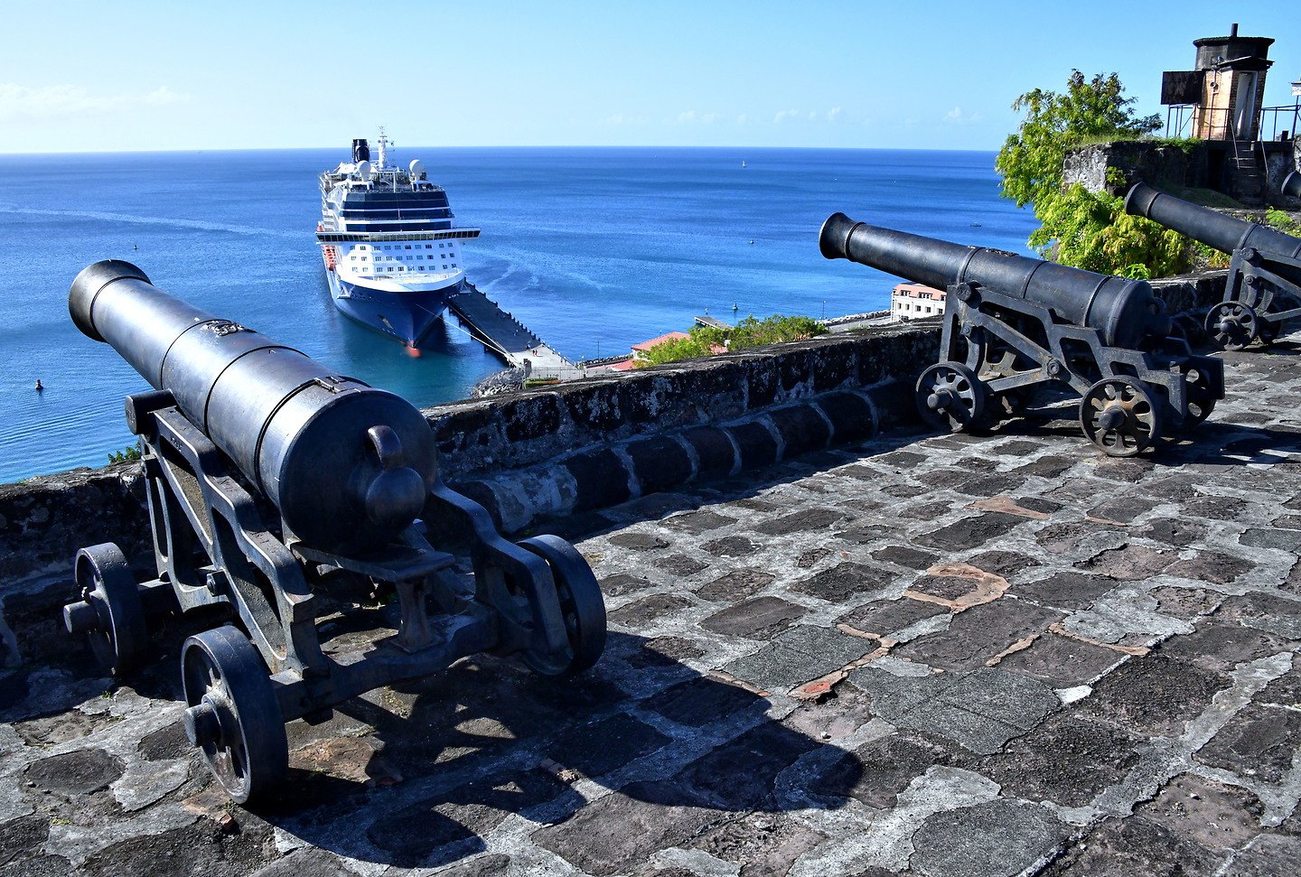 Row of antique iron cannons on a stone fort terrace above a cruise ship in port