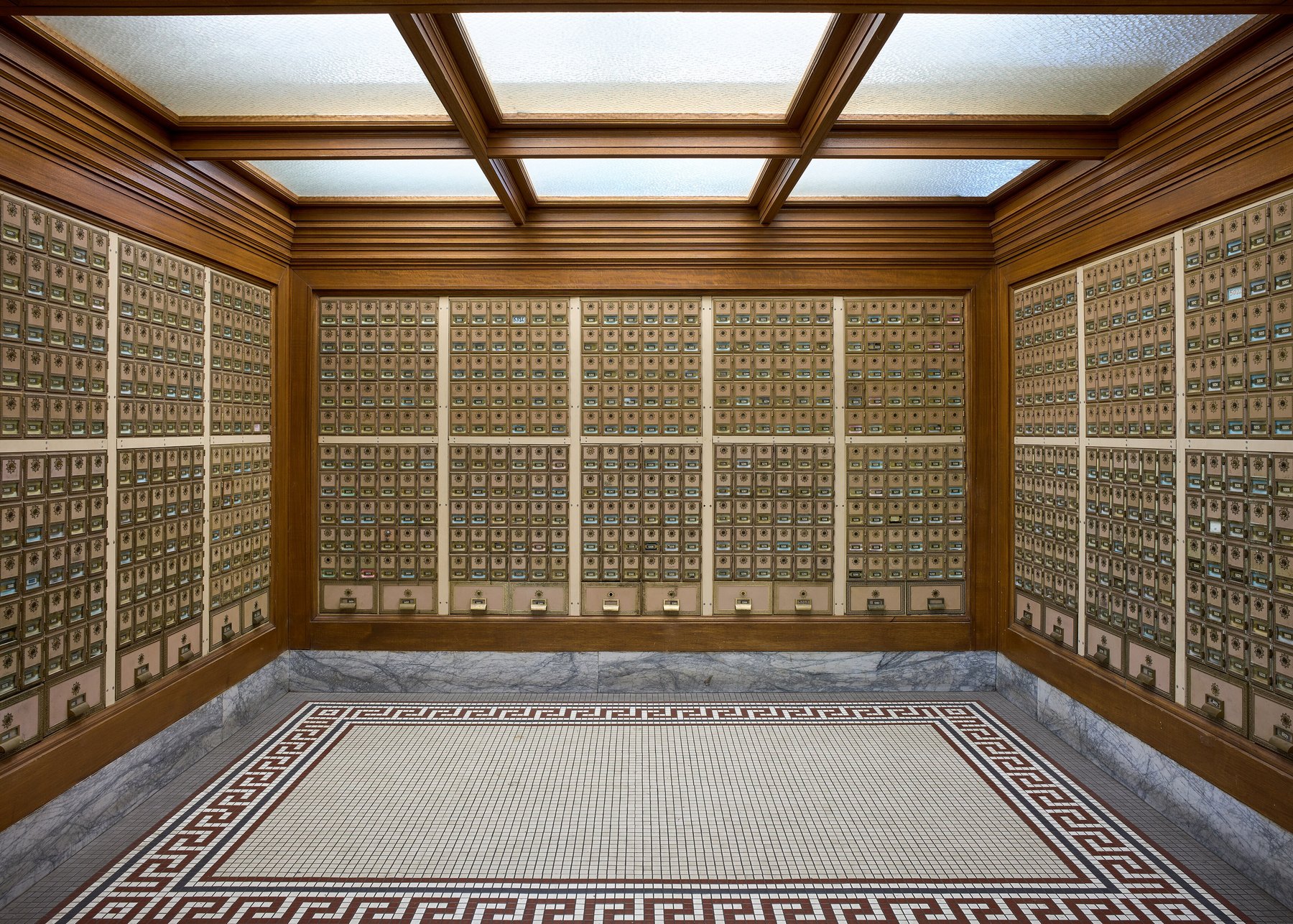 Symmetrical hall of brass post office boxes in wood panelling above a mosaic tile floor