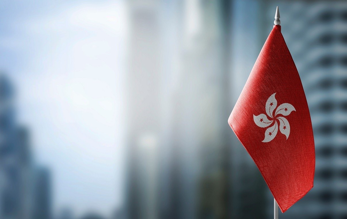 A small Hong Kong flag on a pole against a blurred high-rise skyline