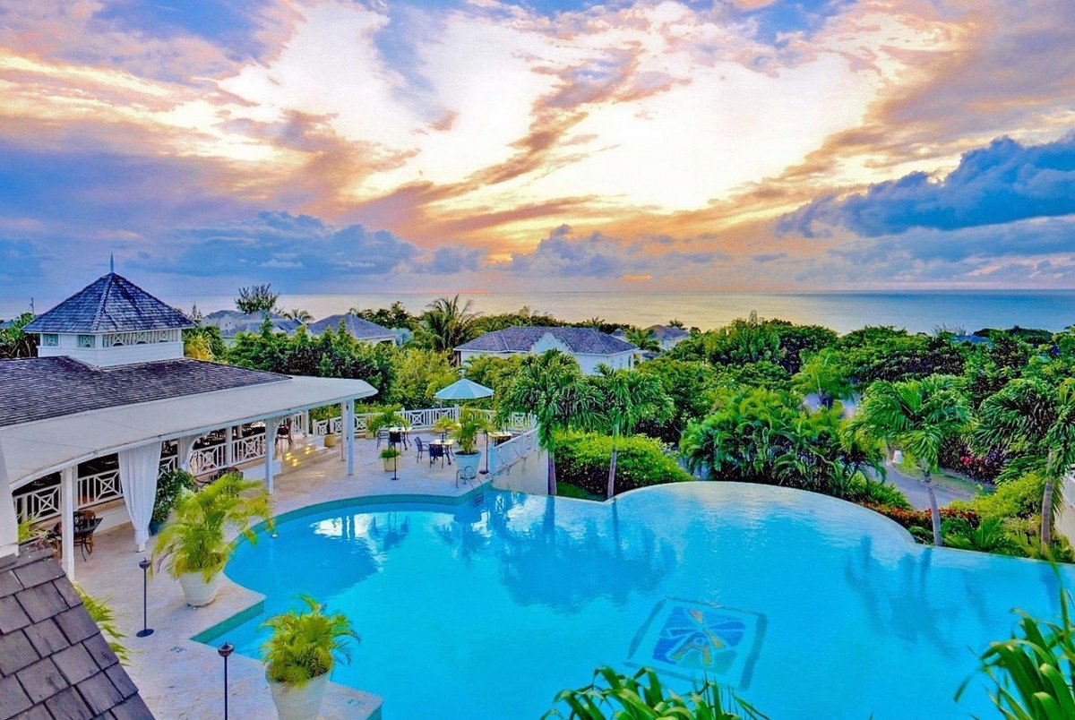 Infinity pool and terrace at a hillside resort under a pink and blue sunset sky