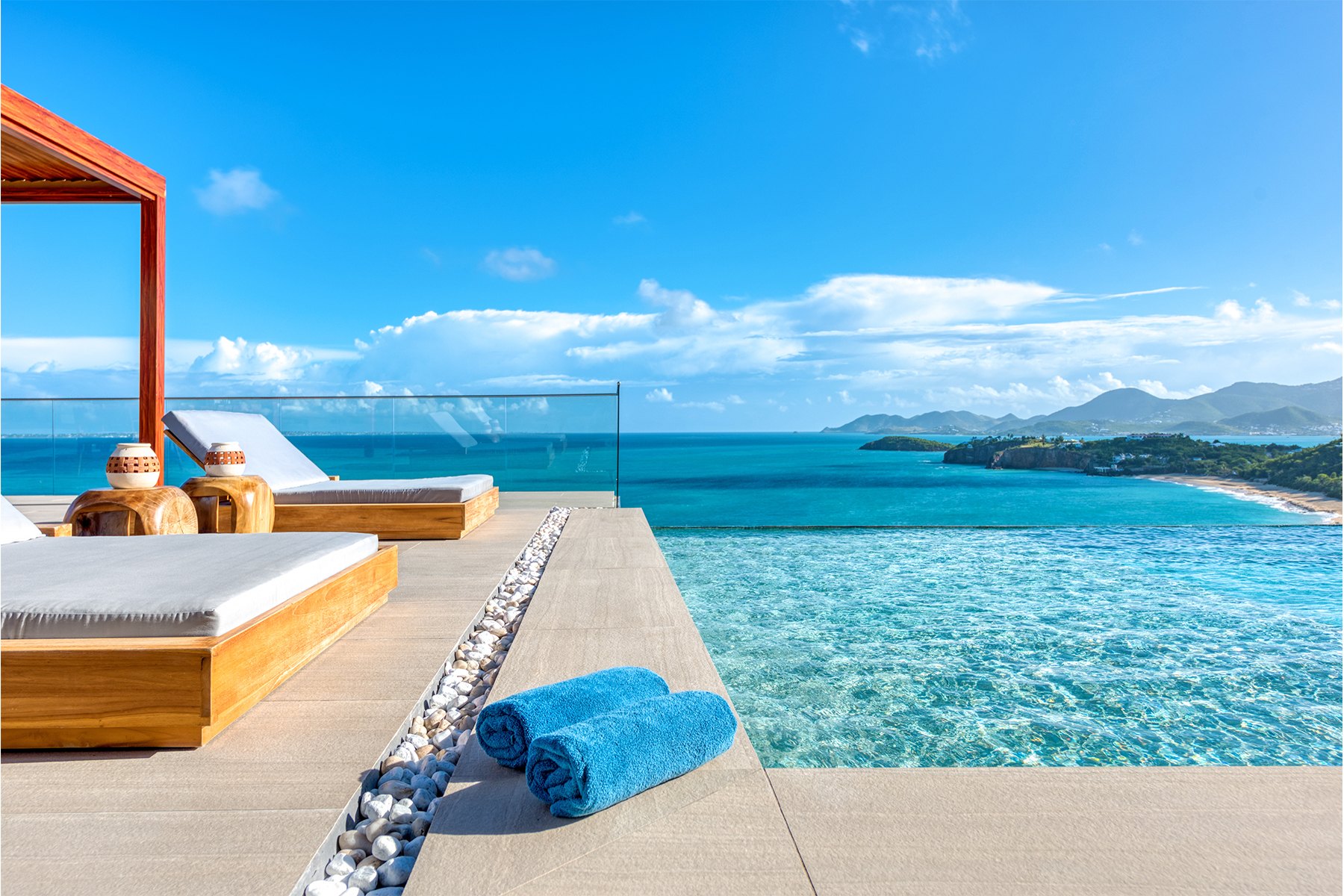 Infinity pool and teak loungers on a terrace overlooking a turquoise bay