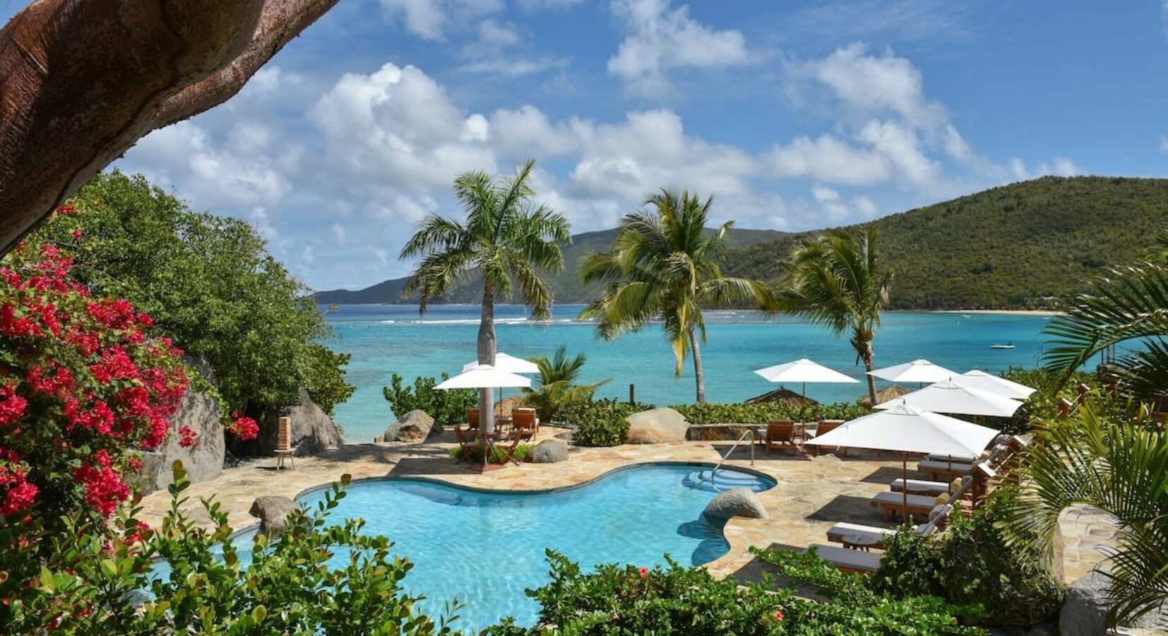 Freeform pool and white umbrellas above the turquoise bay at Rosewood Little Dix Bay