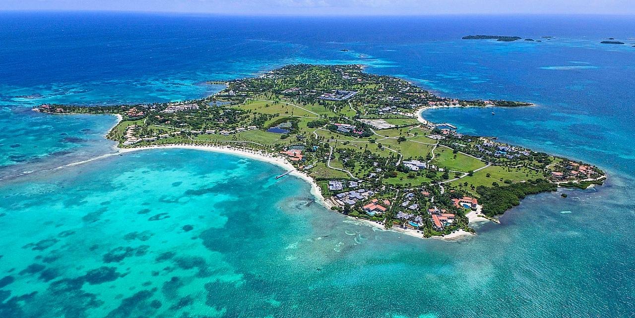 Aerial panorama of a low green peninsula surrounded by shallow turquoise reef water