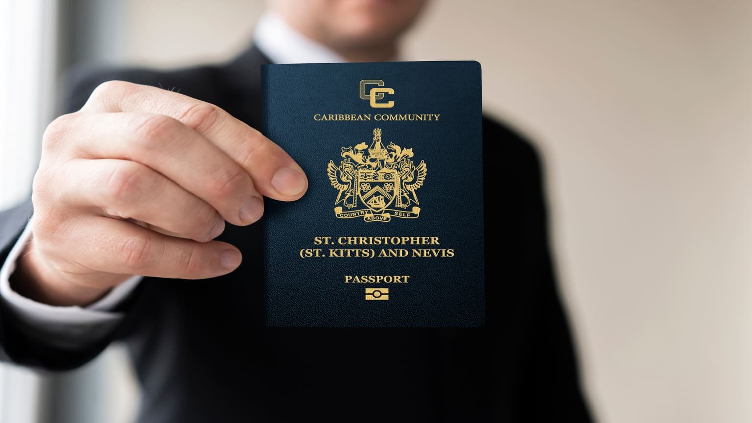 A suited man holds a gold-embossed navy passport toward the camera, face out of frame